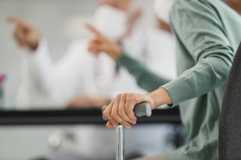 Ältere Person stützt sich mit der Hand auf eine Gehhilfe in einer Pflegeeinrichtung